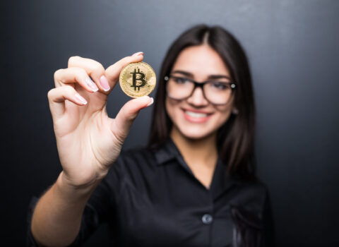 Young successful confident woman with glasses holds a gold bitcoin in her hand isolated on black background